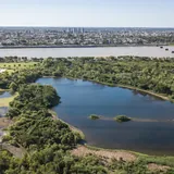 Vista aérea de la Reserva Ecológica UNL en Santa Fe, mostrando la Laguna de las Aves rodeada de bosque nativo, con la laguna Setúbal y la ciudad al fondo.